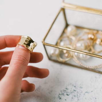 A woman holds a gold ring in front of a jewelry box
