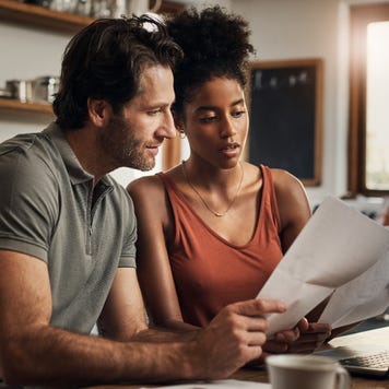 Couple sitting at a kitchen table review documents together, a laptop is open on the table.