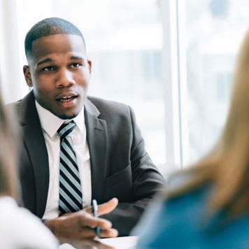 A black financial expert sits in his office with two clients, discussing some financial matters.