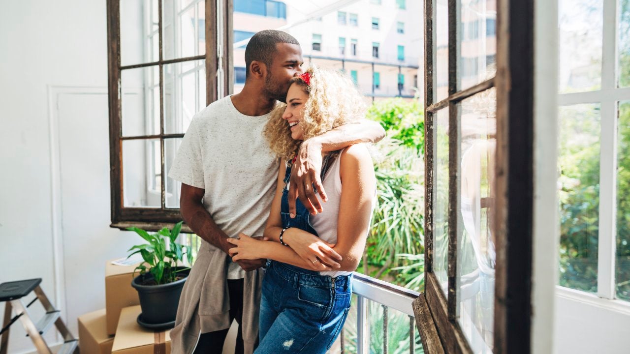 Man kissing woman on the forehead near a window with moving boxes nearby
