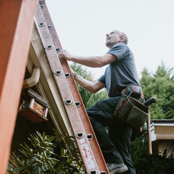 A man on a ladder climbing up to the roof.
