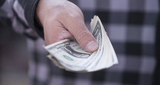 Man in plaid shirt extending hand with dollar bills © Erik Kalibayev/Shutterstock.com