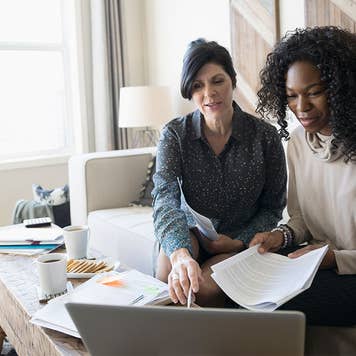 Two women look over paperwork and a computer