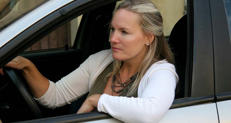 Serious woman on white sweater sitting on driver's seat | iStock.com/LuisPortugal