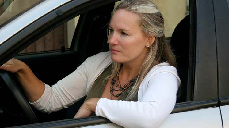 Serious woman on white sweater sitting on driver's seat | iStock.com/LuisPortugal