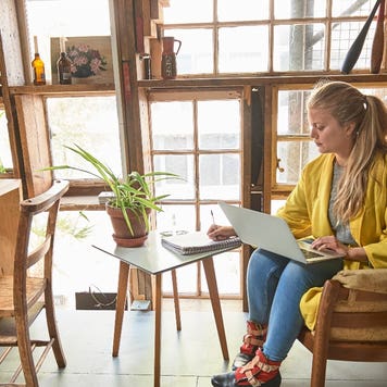 Woman takes notes while working on laptop.