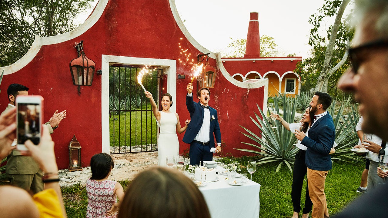 Man and woman holding sparklers to celebrate a wedding outside a red bark.