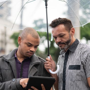 Two people under umbrella using tablet