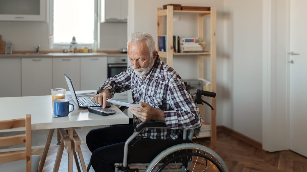 Disabled Senior Man in a Wheelchair Working From Home