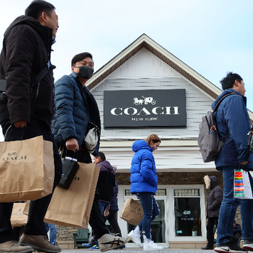 Consumers walking past a Coach store with shopping bags.