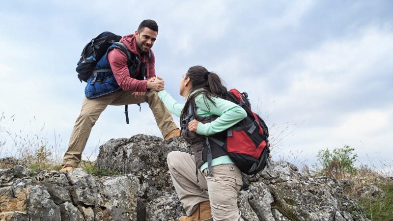 A man helps a woman climb a steep hill while hiking.