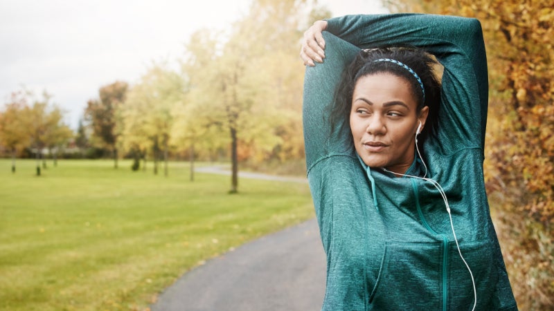 Woman in a green activewear jacket stretching on a trail path