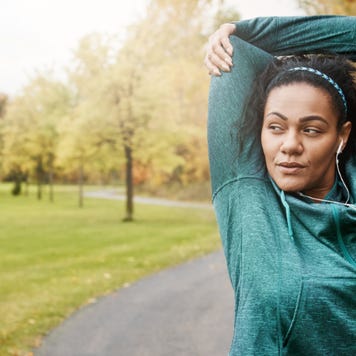 Woman in a green activewear jacket stretching on a trail path