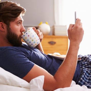 A man sits in bed, looking at his phone.