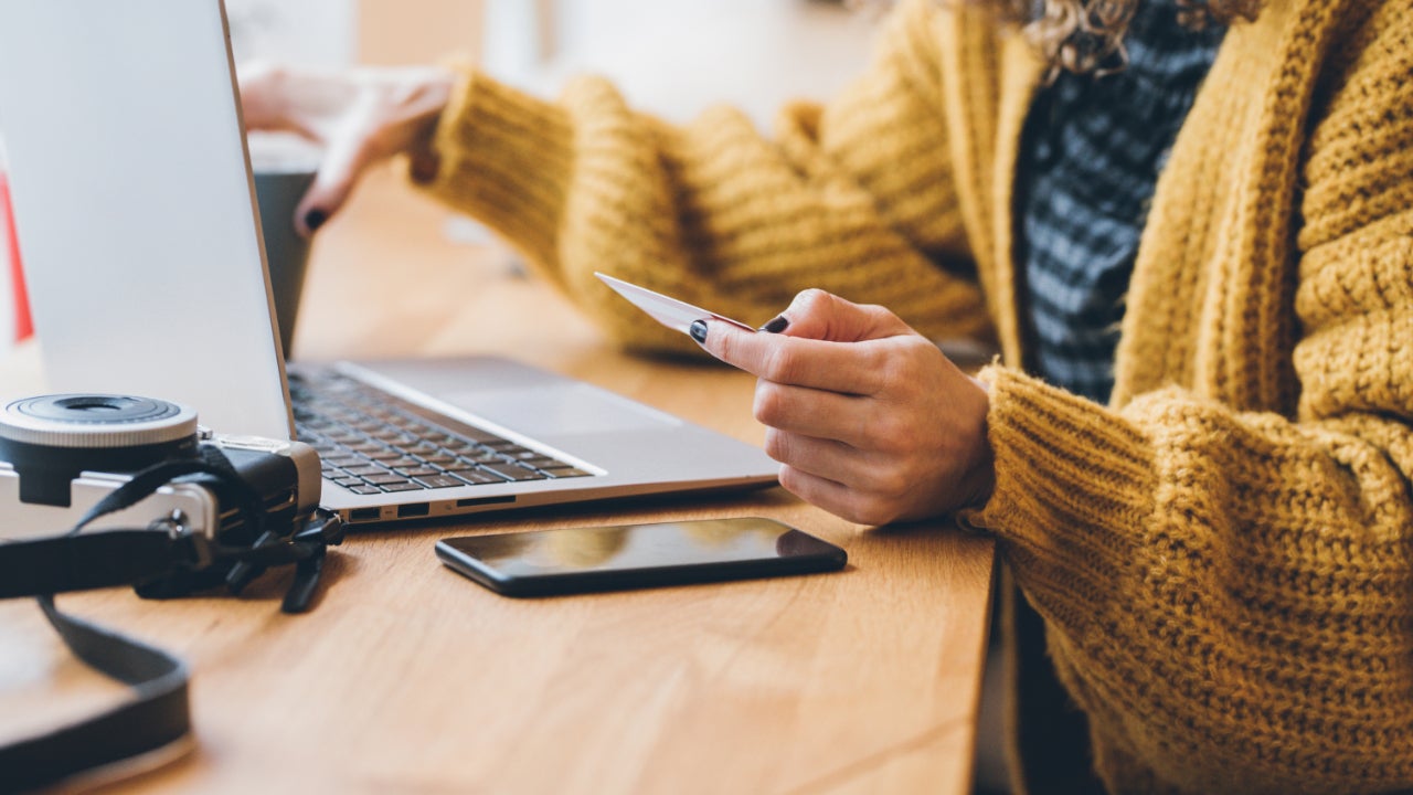 Close-up view of a person leaning over a desk at a laptop and holding a credit card.
