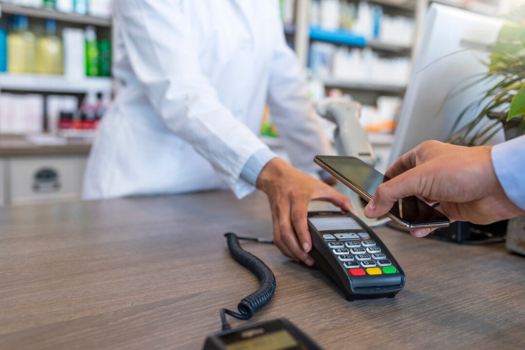 Wireless payment using smartphone and NFC technology. Close up. Male Customer paying with smart phone in pharmacy. Close Up shopping. Modern technology and people concept - Woman with payment terminal and male customer with smartphone paying for medications