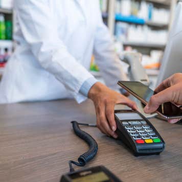 Wireless payment using smartphone and NFC technology. Close up. Male Customer paying with smart phone in pharmacy. Close Up shopping. Modern technology and people concept - Woman with payment terminal and male customer with smartphone paying for medications