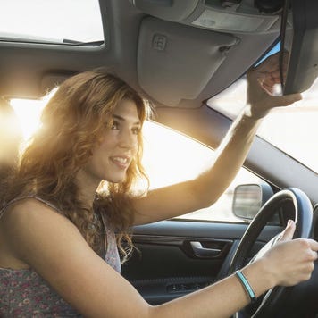A woman adjusts her rearview mirror before she gets ready to drive away.