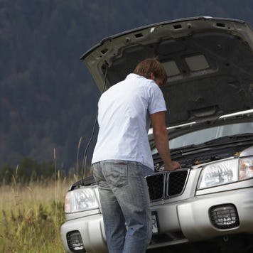 A man stands in front of his car with the hood up trying to get the vehicle fixed.