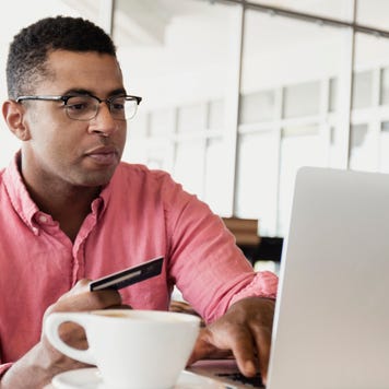 Man in coffee shop using laptop with a card in his hand.