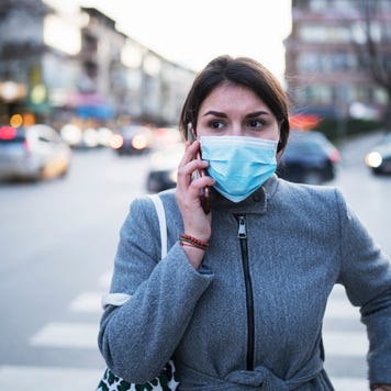 A women wearing a facemask talks on the phone while crossing the street