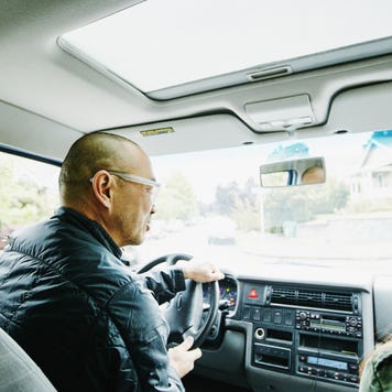 Older Asian man drives his car with his daughter in the passenger seat.