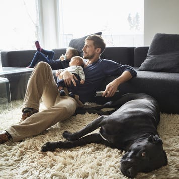 Man sits in the living room on the floor in front of the television with his kids and the family dog.