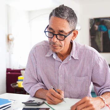 An older man sits down at his table with some papers and a calculator to review his finances after a home insurance claim.