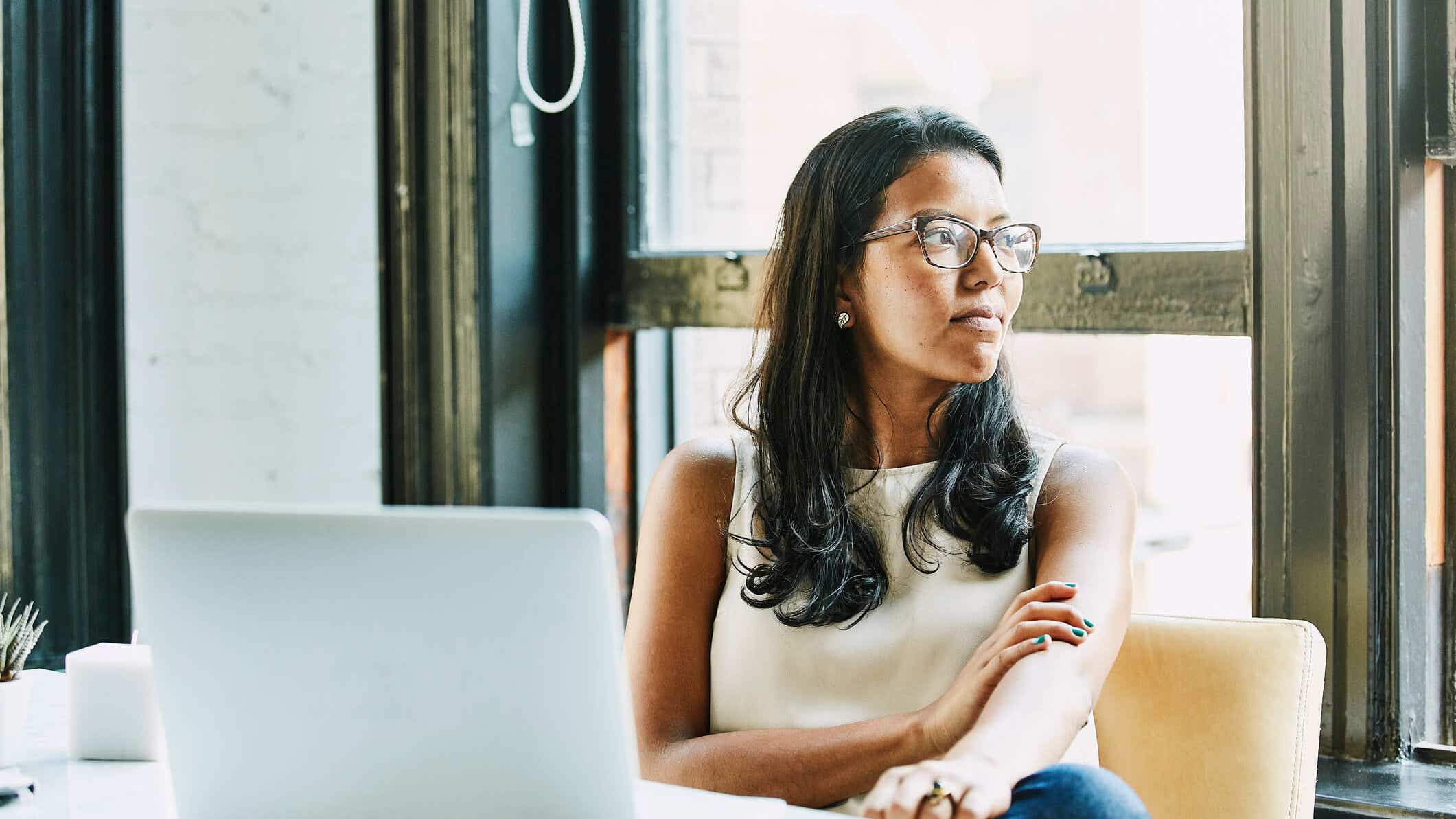 Woman sitting at a table with a laptop in front of her, but she's looking to the right of the photo.