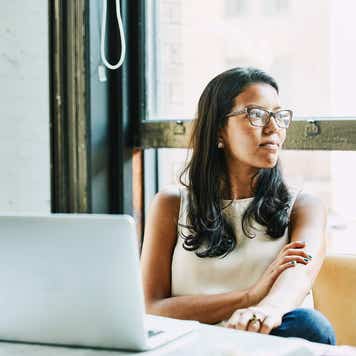 Woman sitting at a table with a laptop in front of her, but she's looking to the right of the photo.