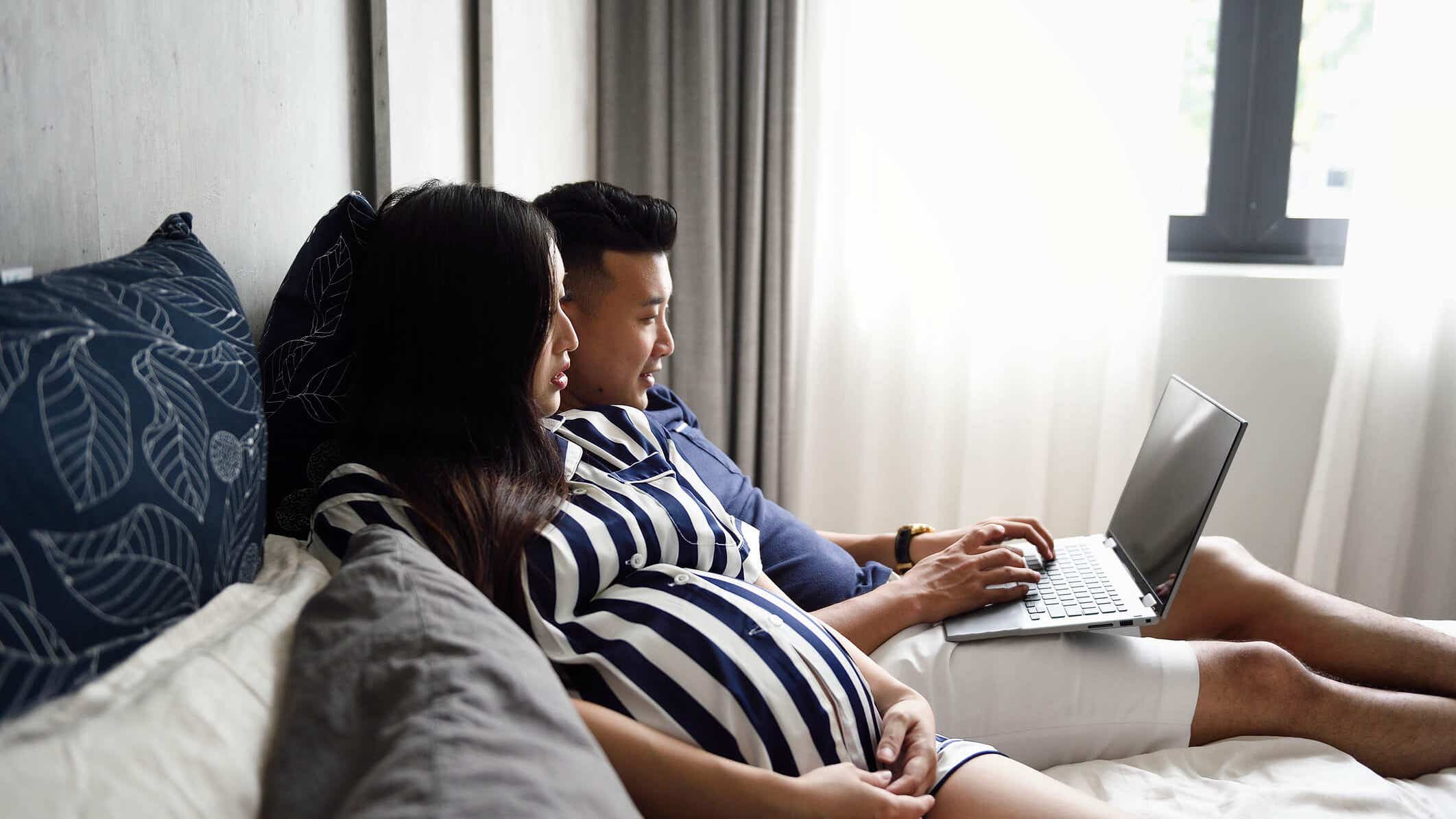 pregnant couple laying down and looking at a laptop