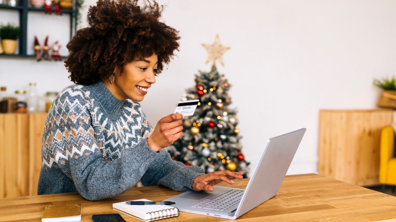 Happy young woman with credit card using laptop sitting at table in living room