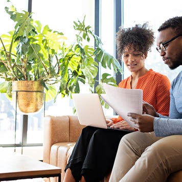 Couple sitting on the couch, reviewing paperwork, and using laptop together