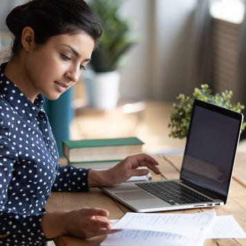 Girl sitting at desk in living room study on laptop making notes