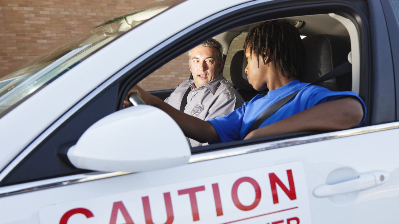 A young black man is in a student driver car with his teacher