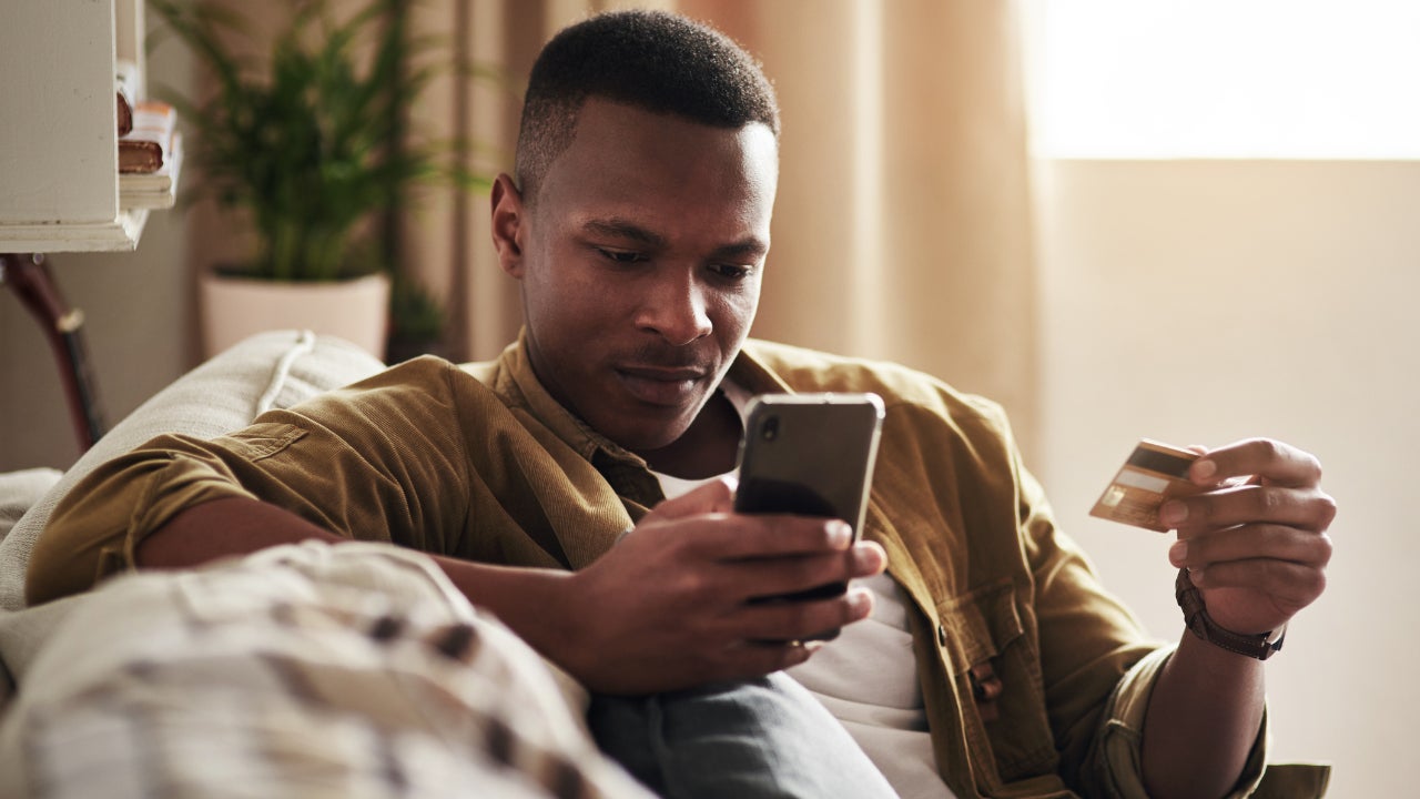 Man closely inspecting smartphone while holding credit card