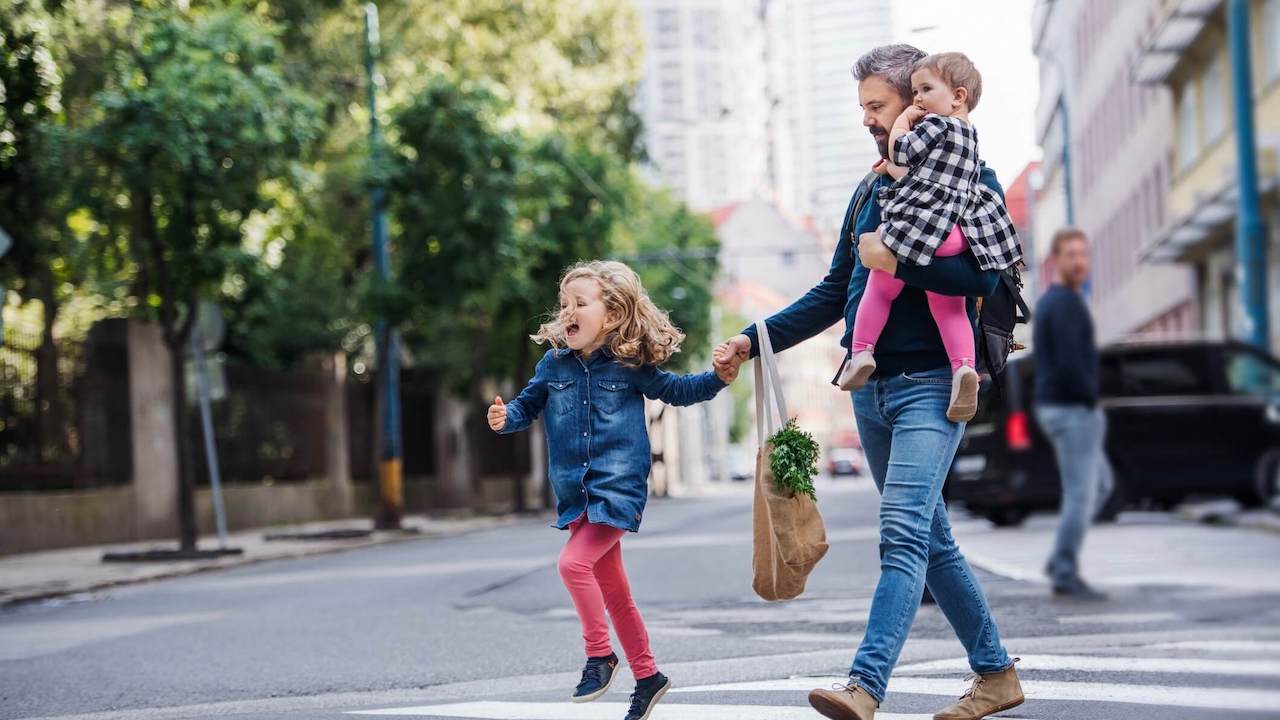 Father with small girls walking outdoors in city, crossing the road