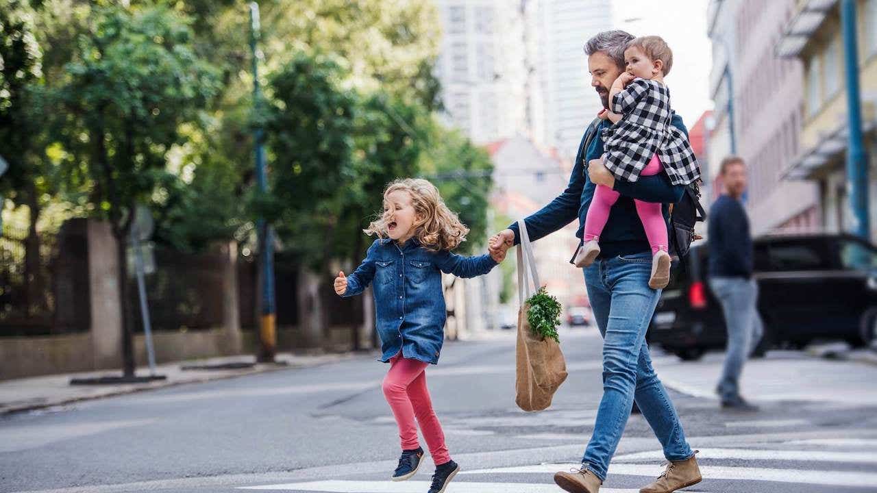 Father with small girls walking outdoors in city, crossing the road
