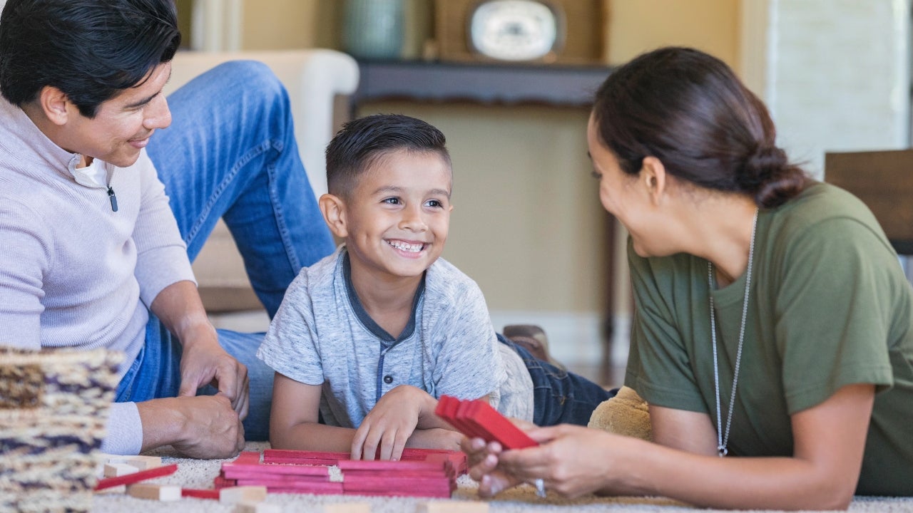 A boy plays with blocks with his parents; his mother is in the military
