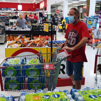 A shopper wearing a protective face mask fills a grocery cart with bottled water at a supermarket.