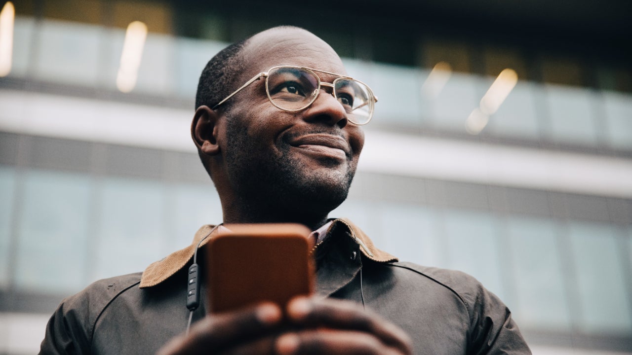 A person with a smartphone smiles and looks into the distance.