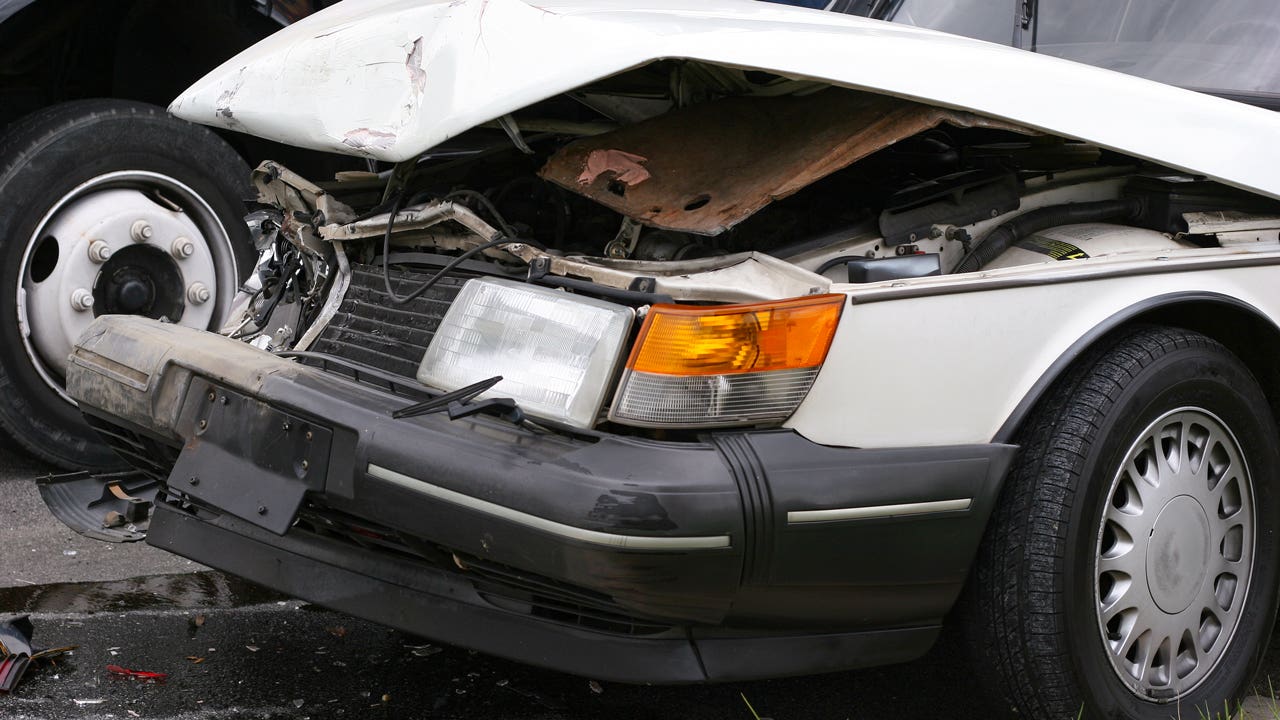 An old white car with the hood bent and crumpled from a collision.