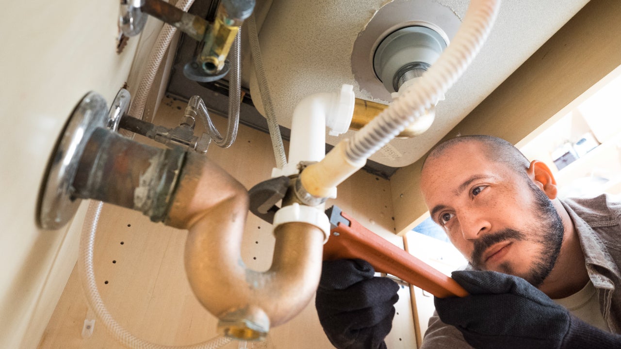 A plumber works under a sink