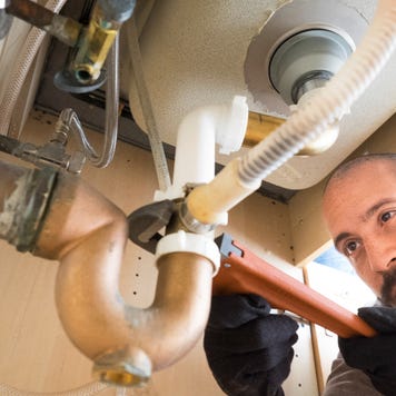 A plumber works under a sink