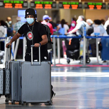 A man pushes his bags on the departures level at Los Angeles International Airport while wearing a mask.