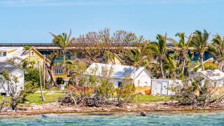 A home on the coast that has been damaged by a hurricane. It is a sunny day.