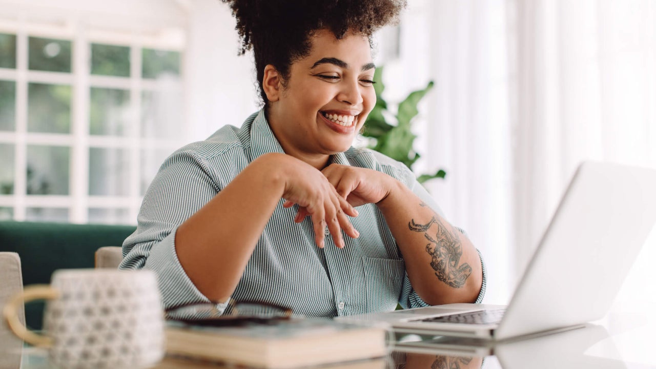 Happy young woman in kitchen smiles widely at her laptop screen