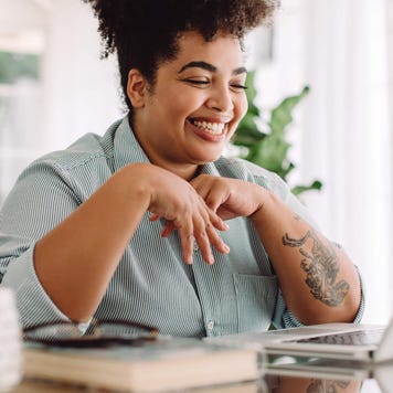 Happy young woman in kitchen smiles widely at her laptop screen