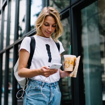 Student walks down the street looking at her phone.
