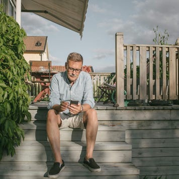Senior man uses smartphone while sitting on his home's back porch step